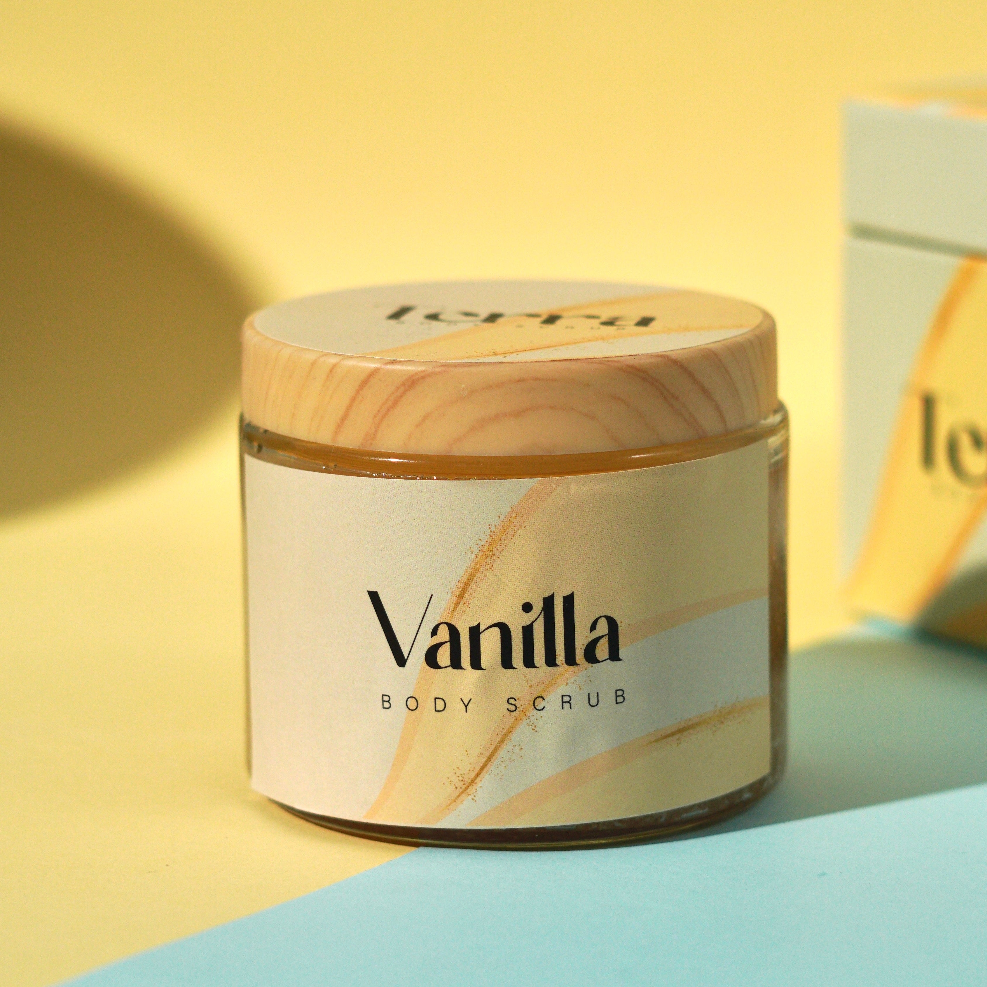 Vanilla body scrub jar with wooden lid on a yellow and blue background
