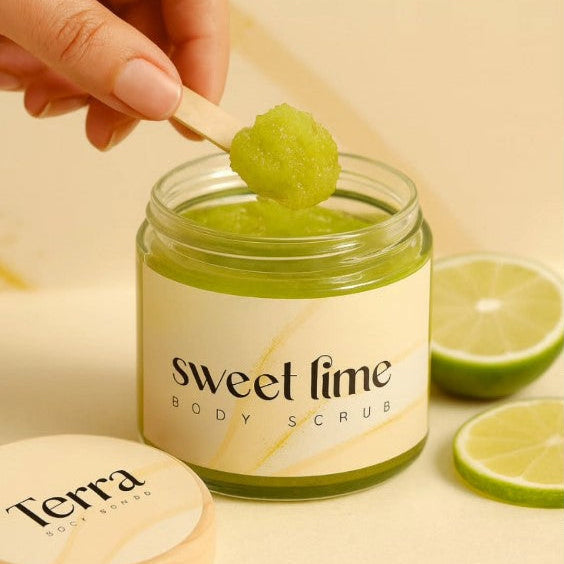 Jar of 'sweet lime' body scrub with a wooden spoon and limes on a beige background