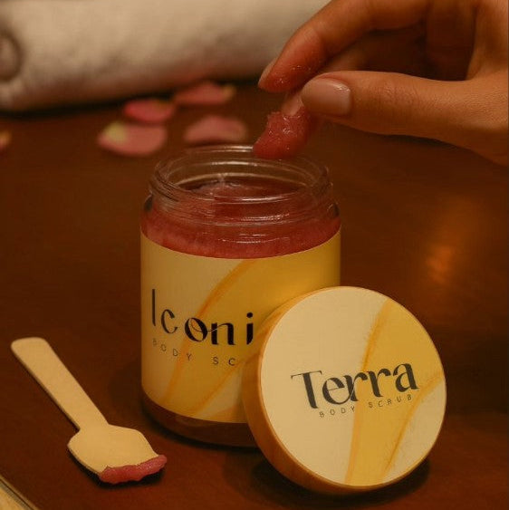 Jar of Terra body scrub with a hand reaching for it on a wooden surface.